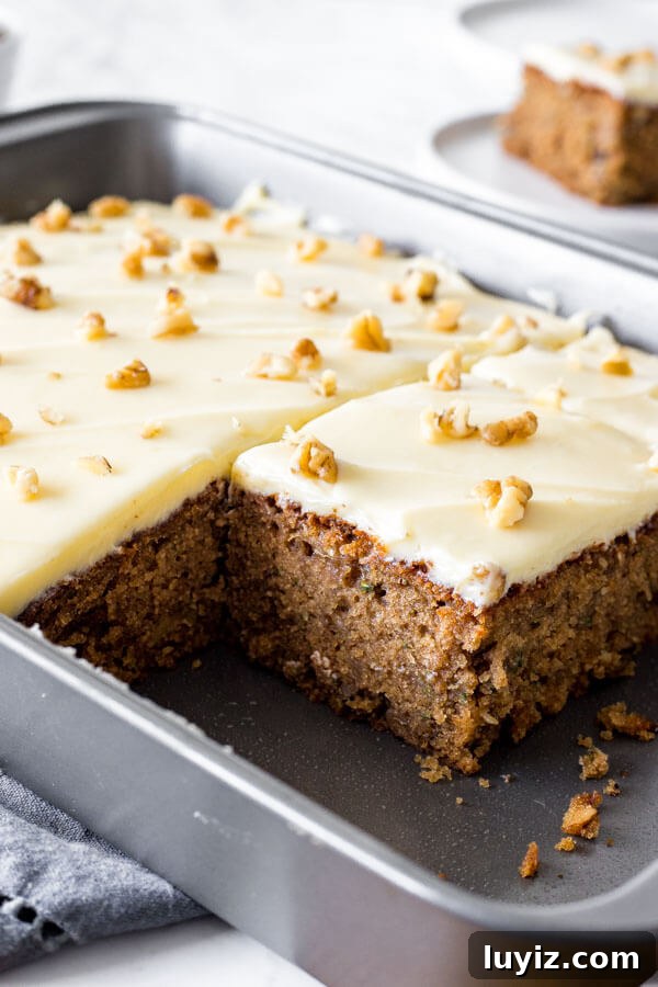 Moist Zucchini Cake Recipe with Cinnamon and Walnuts 3 A 9x13 inch pan of zucchini cake with cream cheese frosting with a close up of a piece that's been cut out from the pan.