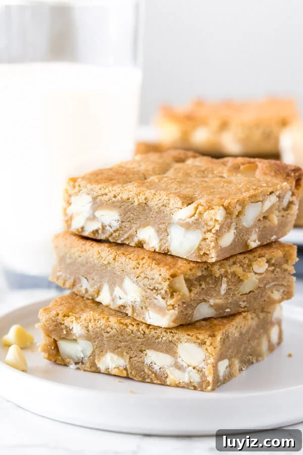 White Chocolate Macadamia Blondie Recipe — Chewy & Decadent 4 A stack of 3 white chocolate macadamia nut blondies with a glass of milk in the background.
