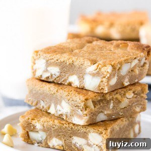 White Chocolate Macadamia Blondie Recipe — Chewy & Decadent 5 A stack of 3 white chocolate macadamia nut blondies with a glass of milk in the background.