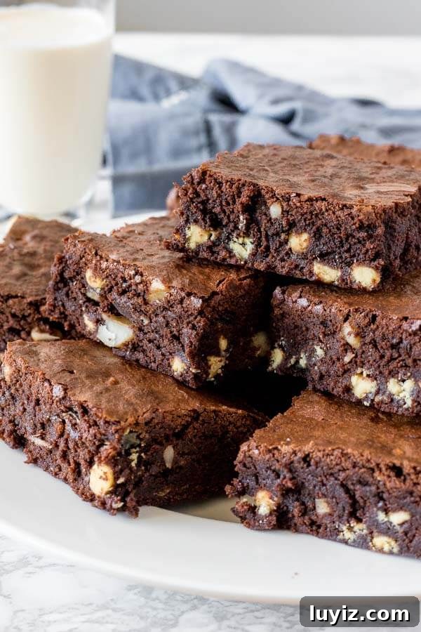 White Chocolate Macadamia Nut Brownies Recipe 3 Chewy, fudgy white chocolate macadamia brownies on a white plate with a glass of milk.