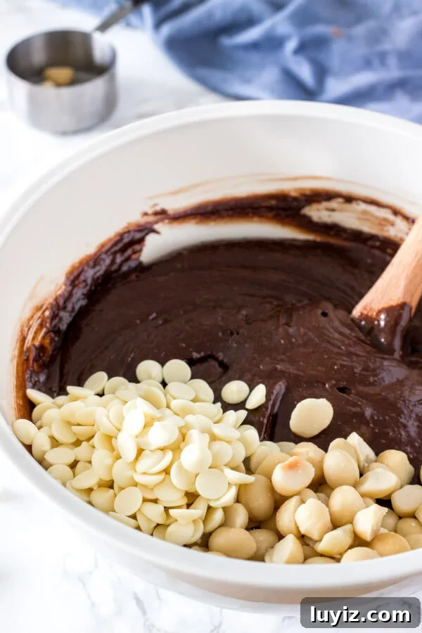 A bowl of brownie batter right before stirring in white chocolate chips and macadamia nuts. 