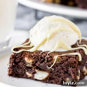 A fudgy white chocolate macadamia nut brownie on a white plate with a scoop of vanilla ice cream to make a brownie sundae.