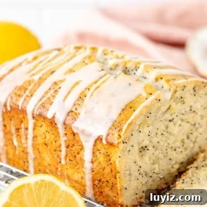 Half of a lemon poppy seed loaf drizzled with lemon glaze on a cooling rack
