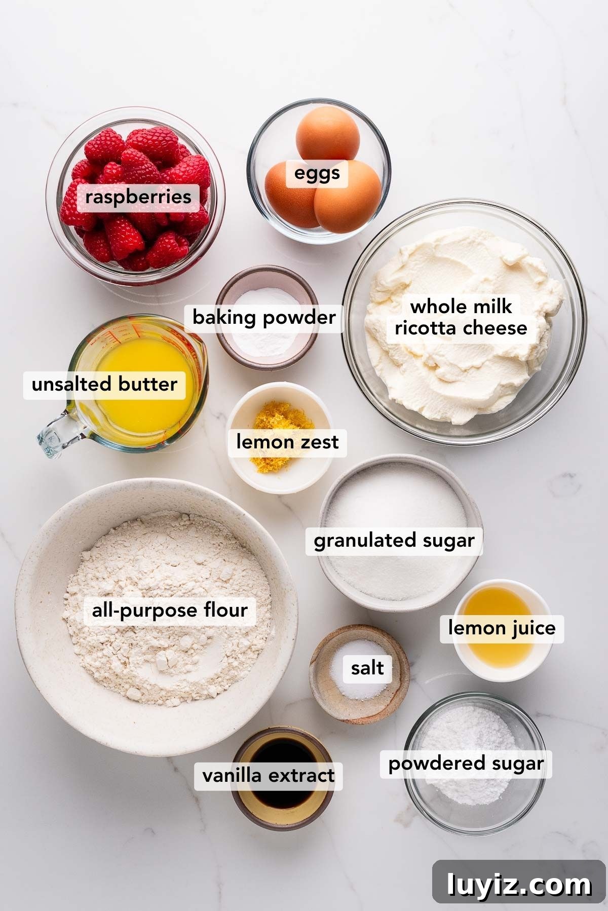 Lemon Raspberry Ricotta Cake Recipe — Moist Spring Dessert 4 Labeled ingredients in bowls used to make lemon raspberry ricotta cake on a white marbled background.