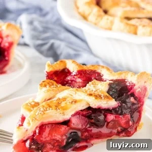 A slice of mixed berry pie with strawberries, blueberries and raspberries in the filling with a flaky lattice top crust.