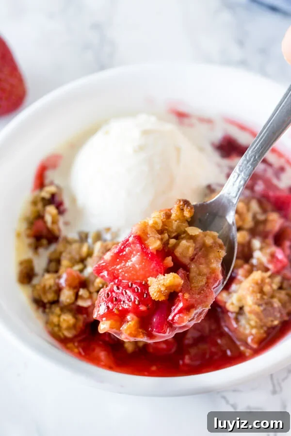 Strawberry Rhubarb Crisp Recipe with Buttery Oat Topping 5 Close up of a spoonful of strawberry rhubarb crisp with juicy pieces of fruit and oatmeal crumble.