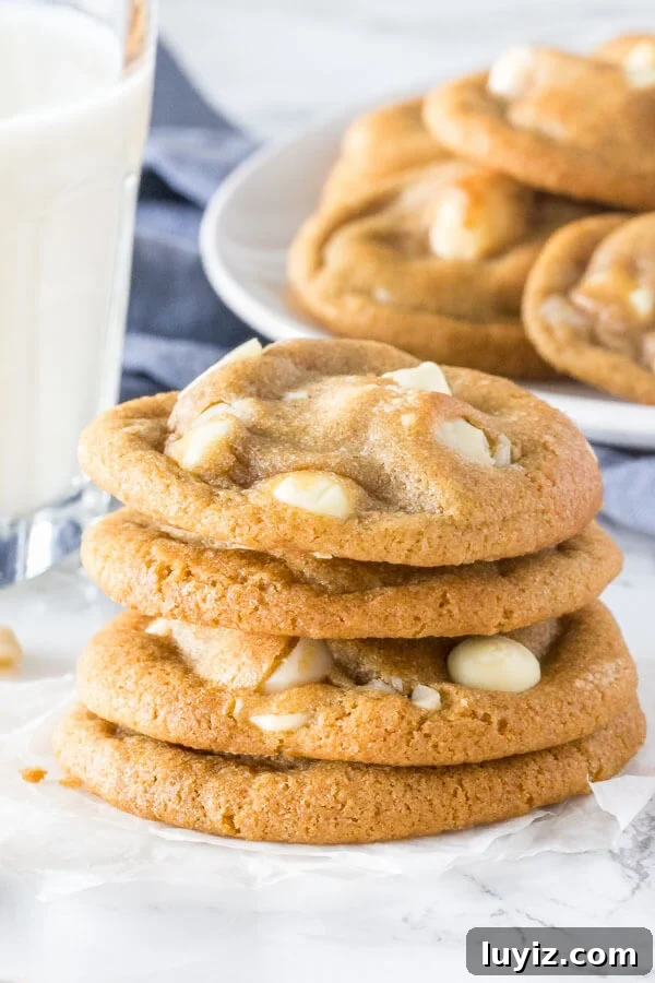 White Chocolate Macadamia Nut Cookies Recipe 2 A stack of soft, chewy white chocolate macadamia cookies with golden edges. With a glass of milk and extra plate of cookies in the background.