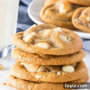 White Chocolate Macadamia Nut Cookies Recipe 6 A stack of soft, chewy white chocolate macadamia cookies with golden edges. With a glass of milk and extra plate of cookies in the background.