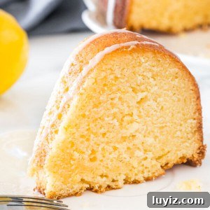 A slice of moist lemon bundt cake with a drizzle of lemon glaze on a white plate.