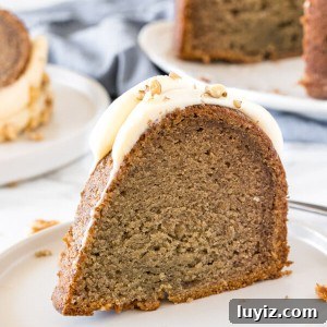 Moist Banana Bundt Cake Recipe with Cinnamon Glaze 6 A slice of banana bundt cake with cream cheese frosting on a white plate.