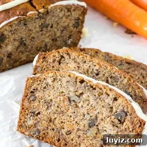 Close up of 3 slices of banana carrot bread with the rest of the loaf and 2 carrots to show the moist crumb.