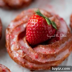 Strawberry-Glazed French Crullers Recipe for Homemade Pastries 13 Strawberry glazed french crullers on a parchment paper lined baking sheet topped with a fresh strawberry.