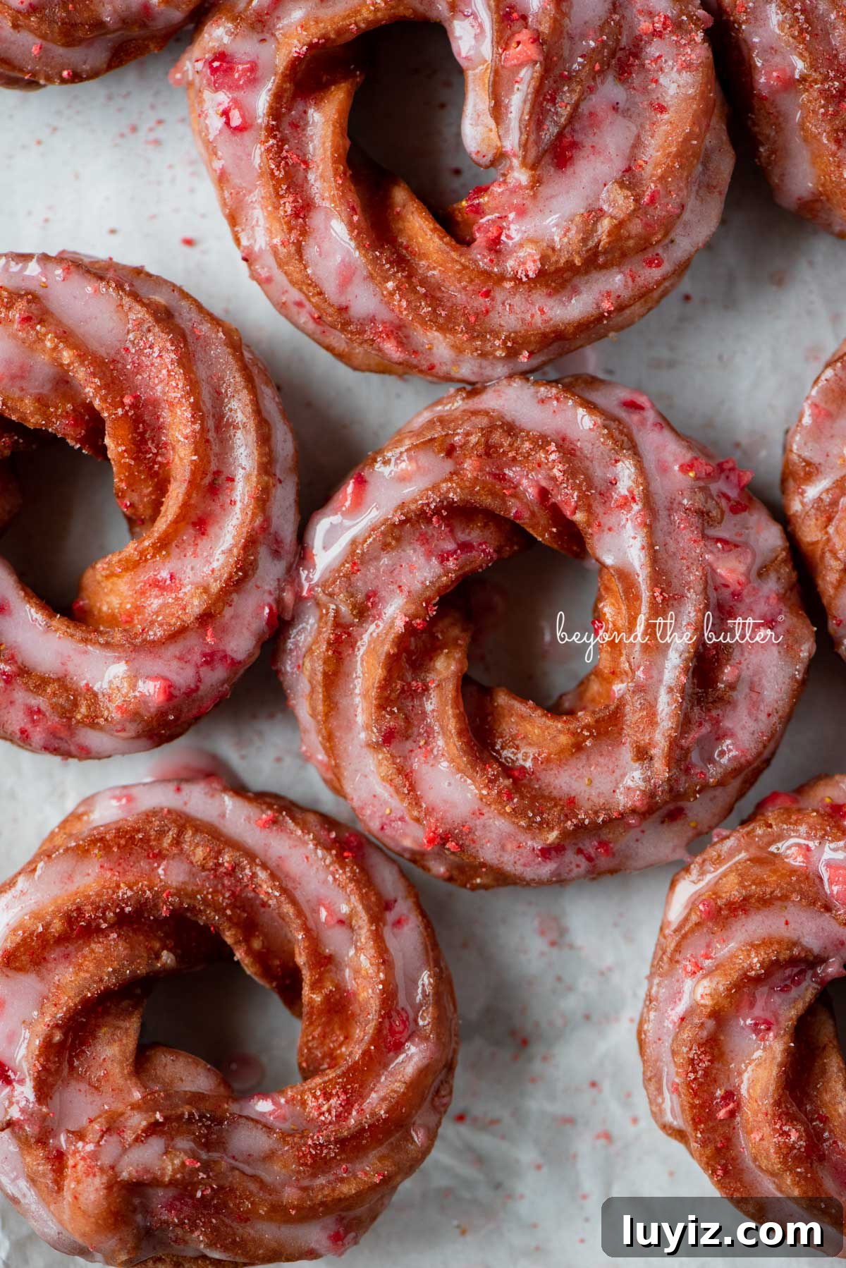 Strawberry-Glazed French Crullers Recipe for Homemade Pastries 3 Strawberry glazed french crullers sprinkled with strawberry sugar on a parchment paper lined baking sheet | © Beyond the Butter®
