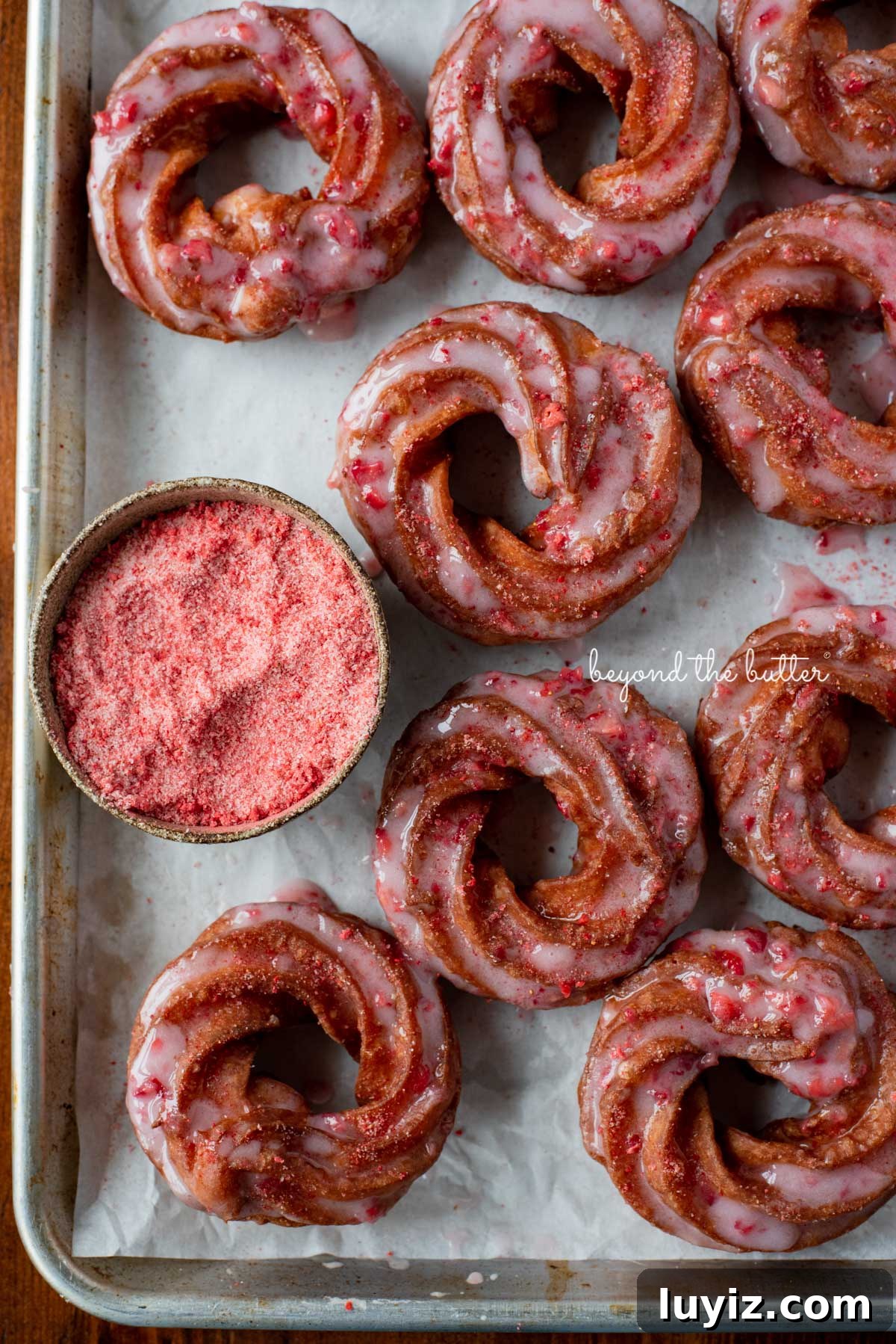 Strawberry-Glazed French Crullers Recipe for Homemade Pastries 7 Strawberry glazed french crullers sprinkled with strawberry sugar on a parchment paper lined baking sheet | © Beyond the Butter®