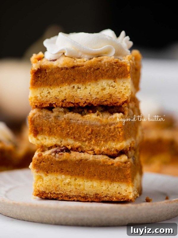 Pumpkin Fudge Brownies with Creamy Frosting 10 Stack of three pumpkin pie cake bars on a parchment paper lined bottom.