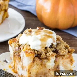 A slice of pumpkin French toast casserole with streusel topping with whipped cream and maple syrup to serve