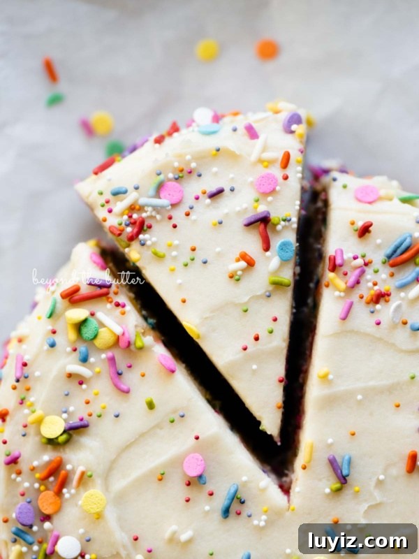 Cut slice of single layer funfetti cake partially removed from rest of the cake on white parchment paper.