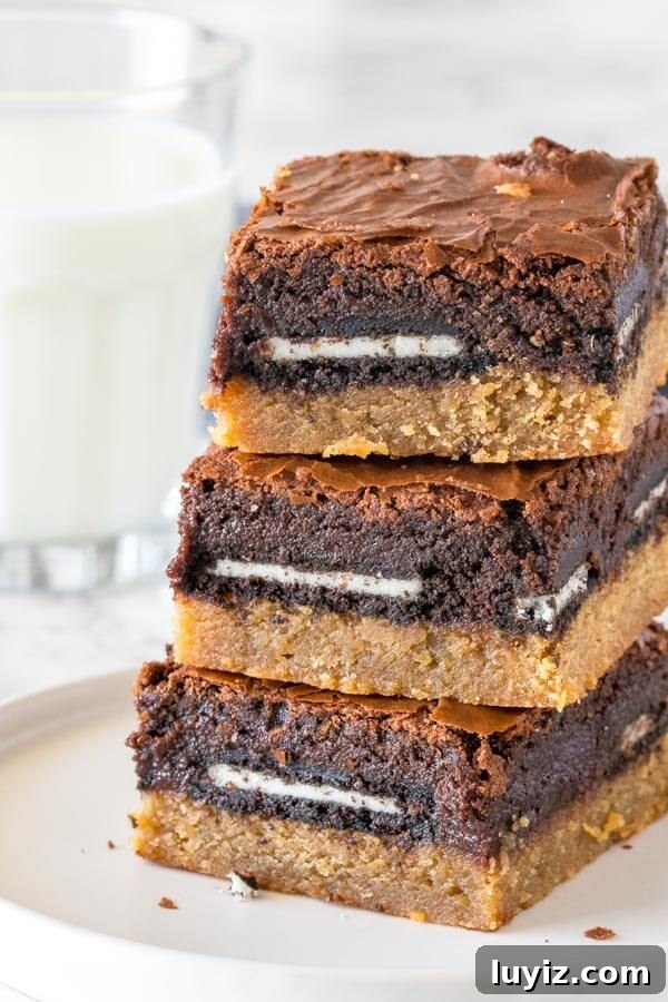 Decadent Peanut Butter Brownies with Oreo Swirls 2 A stack of 3 peanut butter slutty brownies taken from the side to show the peanut butter cookie bottom, Oreo middle and brownie top layer.