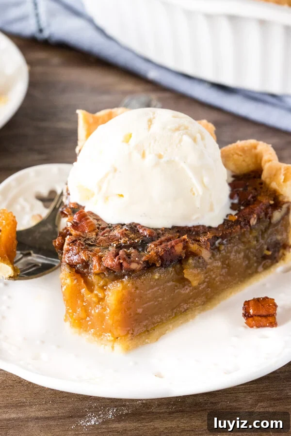 Classic Southern Pecan Pie Recipe with Buttery Pecan Topping 6 A slice of pecan pie with a scoop of ice cream on top and a bite taken out to show the chewy texture.