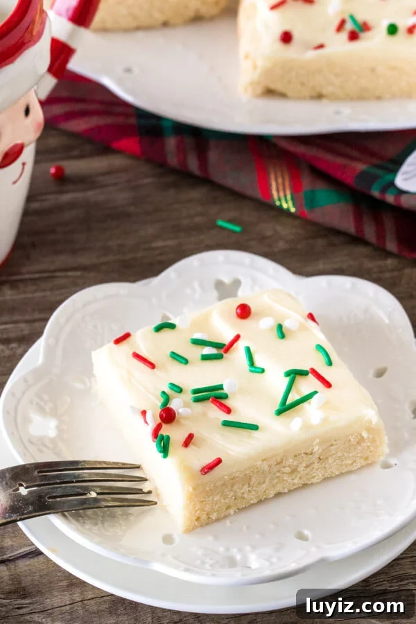 Christmas Sugar Cookie Bar Recipe — Festive, Soft & Chewy 2 A Christmas sugar cookie bar on a white plate with frosting and green and red sprinkles.