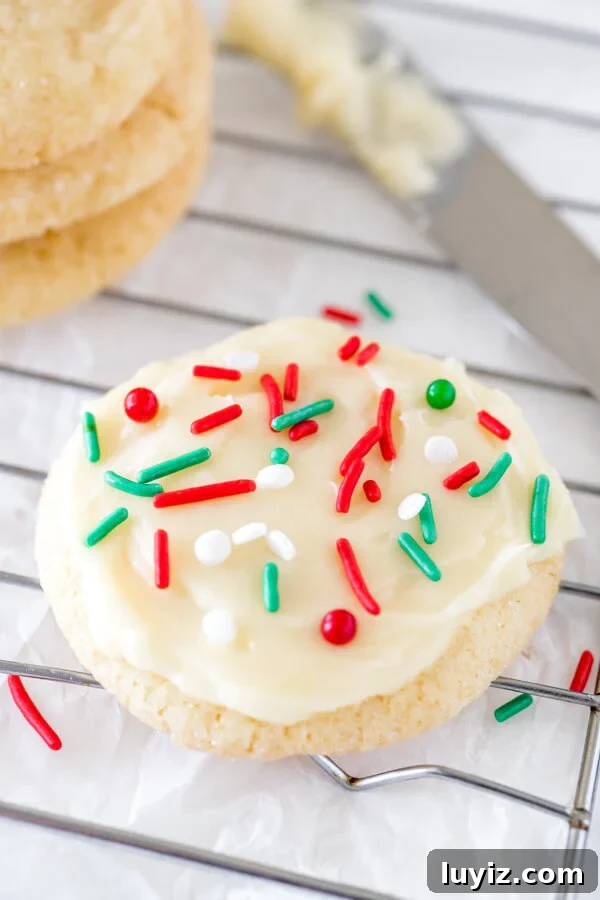 A round sugar cookie with white frosting and Christmas sprinkles on a cooling rack.