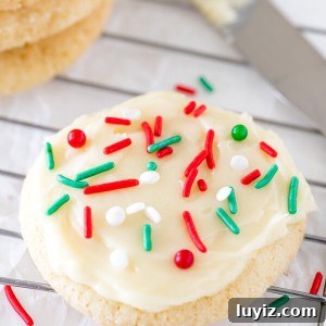 A round sugar cookie with white frosting and Christmas sprinkles on a cooling rack.