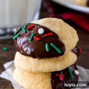 A stack of 3 chocolate dipped shortbread cookies with a glass of milk