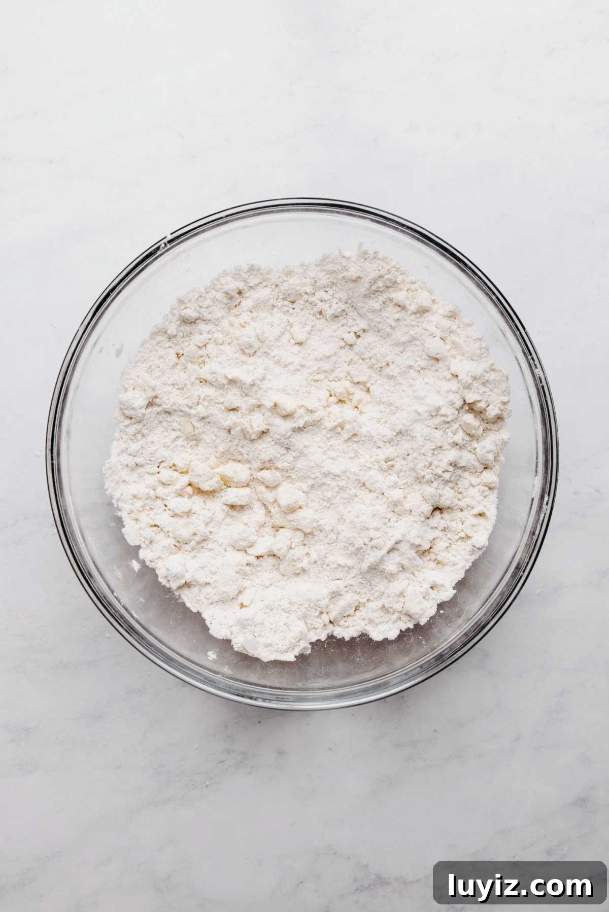 Crispy Chocolate Chip Scones with Vanilla Glaze 6 Butter cut into flour mixture in large glass mixing bowl on a white and grey marbled background.