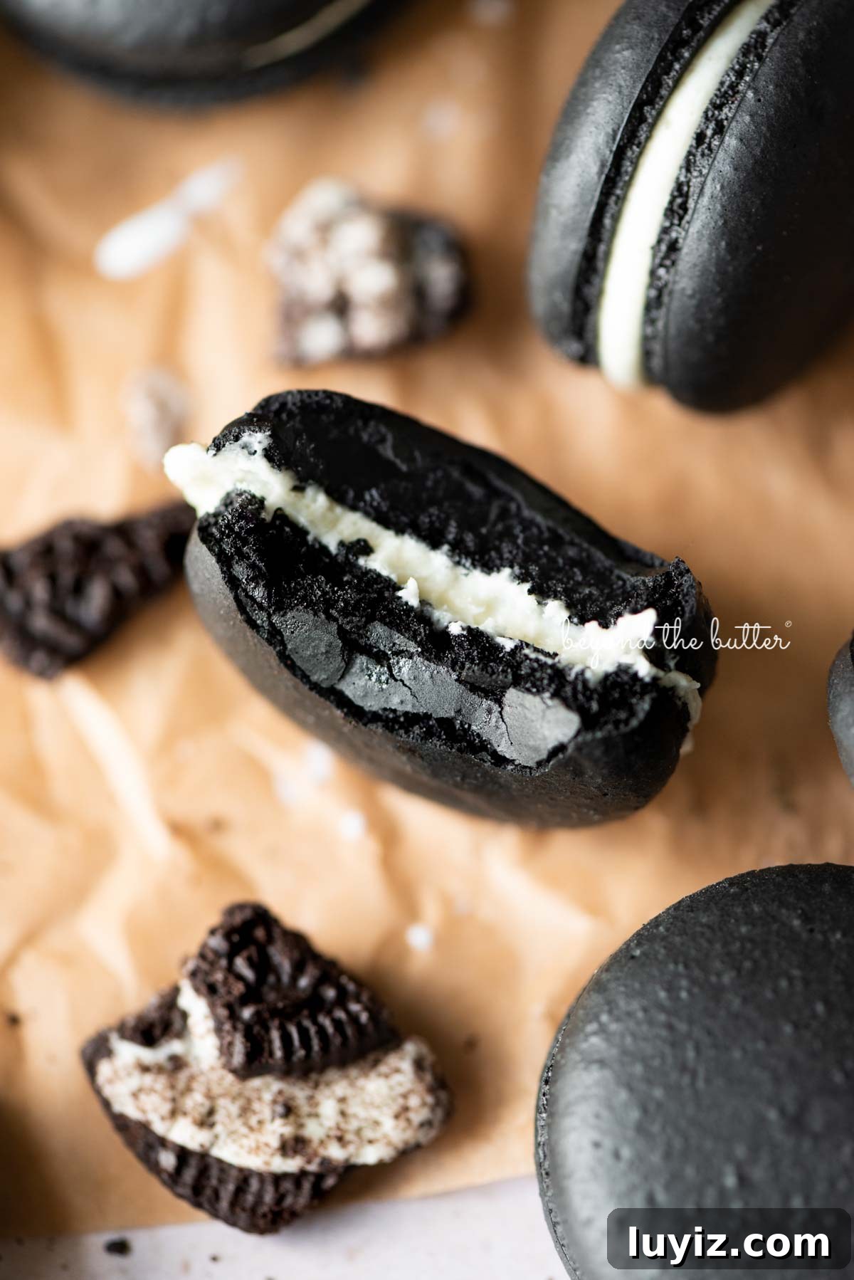 Oreo Cookie Macarons: Step-by-Step Recipe for Perfect Bites 2 Half eaten oreo macaron on parchment paper surrounded by oreo macarons and broken pieces of oreo cookies.