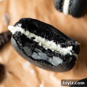 Oreo Cookie Macarons: Step-by-Step Recipe for Perfect Bites 11 Half eaten oreo macaron on parchment paper surrounded by oreo macarons and broken pieces of oreo cookies.
