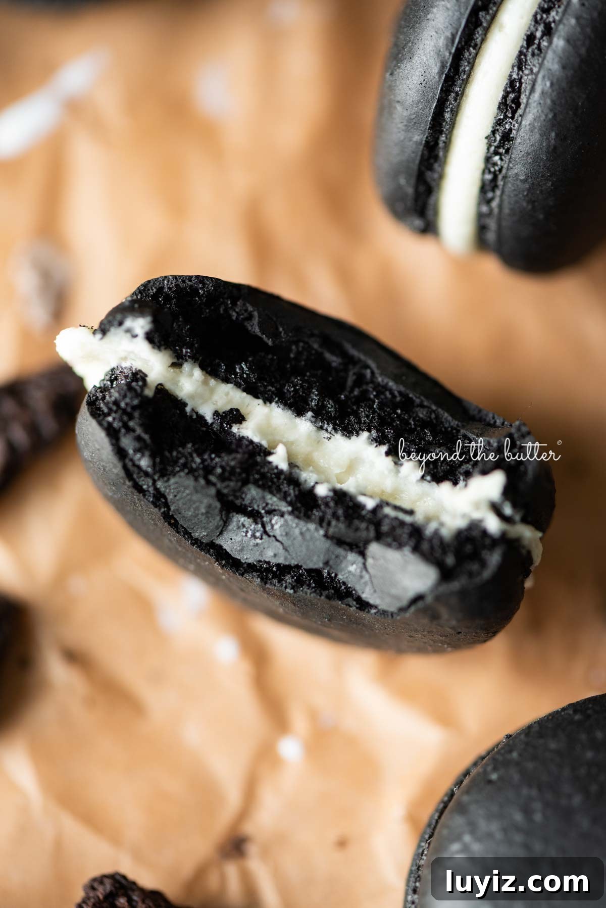 Oreo Cookie Macarons: Step-by-Step Recipe for Perfect Bites 6 Half eaten oreo macaron on parchment paper surrounded by oreo macarons and broken pieces of oreo cookies
