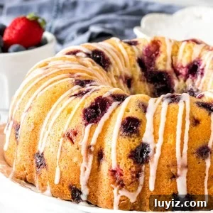 A berry bundt cake on a plate with a drizzle of glaze on top