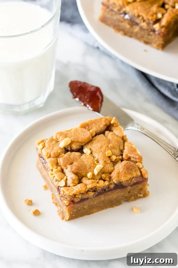 Peanut Butter and Jelly Bars Recipe — Chewy Jam-Filled Squares 5 Peanut butter and jelly square on a plate with a glass of milk.