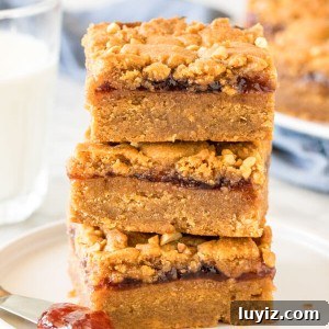 Peanut Butter and Jelly Bars Recipe — Chewy Jam-Filled Squares 6 Stack of 3 peanut butter and jelly bars with a glass of milk.