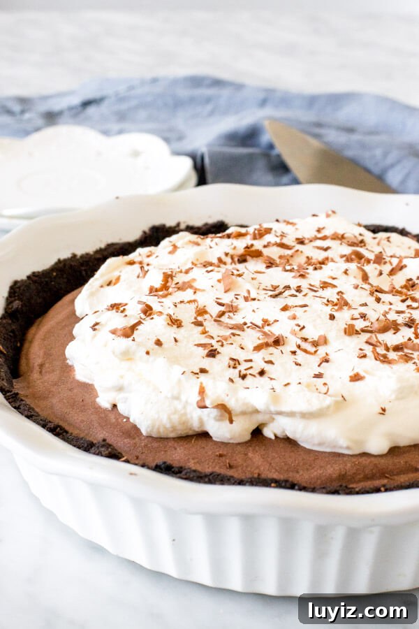 Decadent Chocolate Mousse Pie Recipe with Silky Ganache 2 Chocolate mousse pie with Oreo crust and whipped cream topping in a white pie plate.