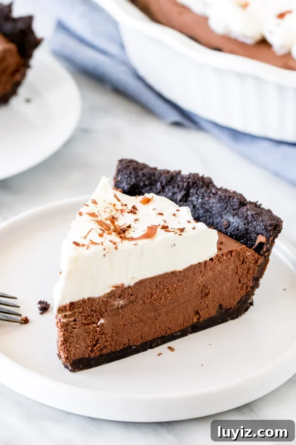Decadent Chocolate Mousse Pie Recipe with Silky Ganache 3 Slice of chocolate mousse pie with whipped cream on a white plate.