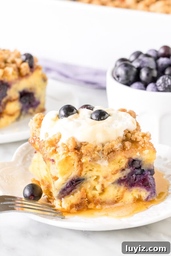 Blueberry French Toast Casserole Recipe for Brunch and Holidays 2 Slice of blueberry French toast casserole with whipped cream on top and drizzled in syrup. Bowl of blueberries and second piece in the background.