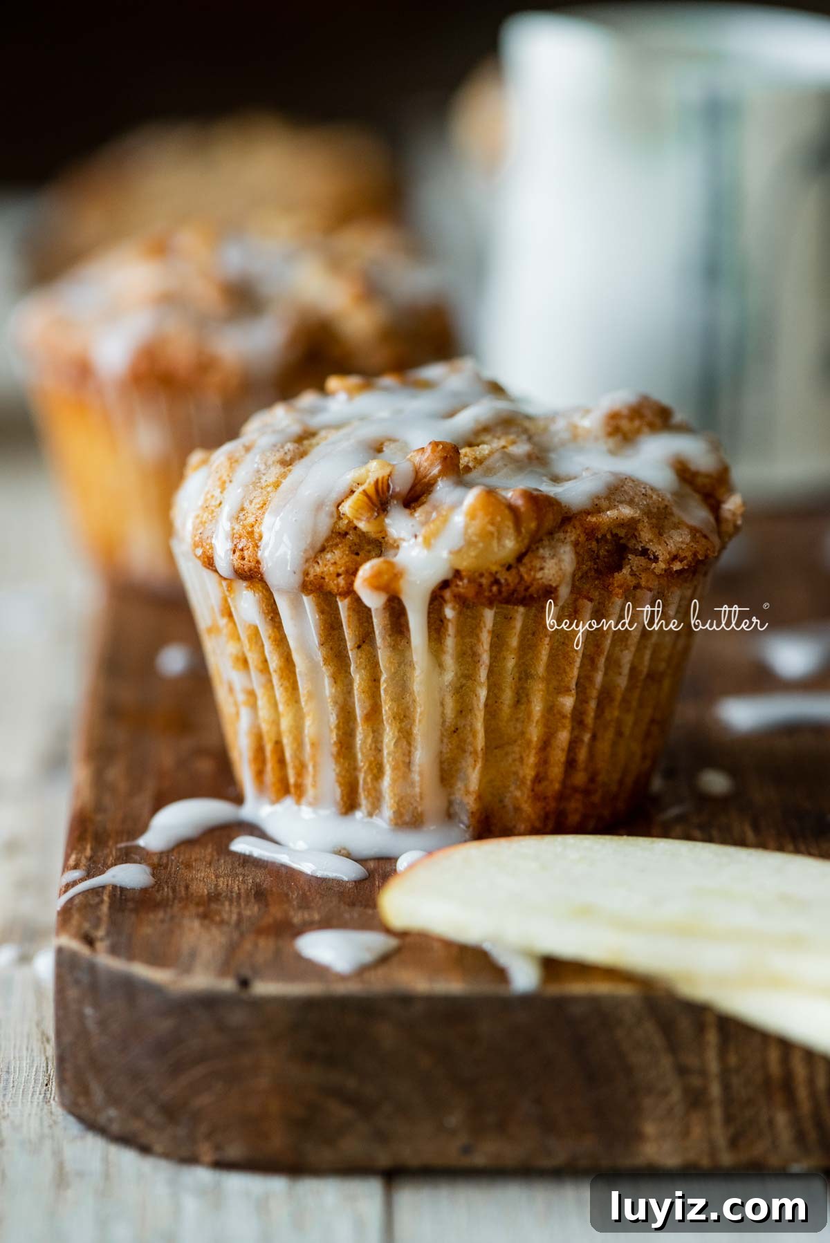 Apple Cinnamon Streusel Muffins Recipe with Crunchy Topping 2 Warm apple cinnamon streusel muffins on a wood cutting board with slices of apples and vanilla glaze