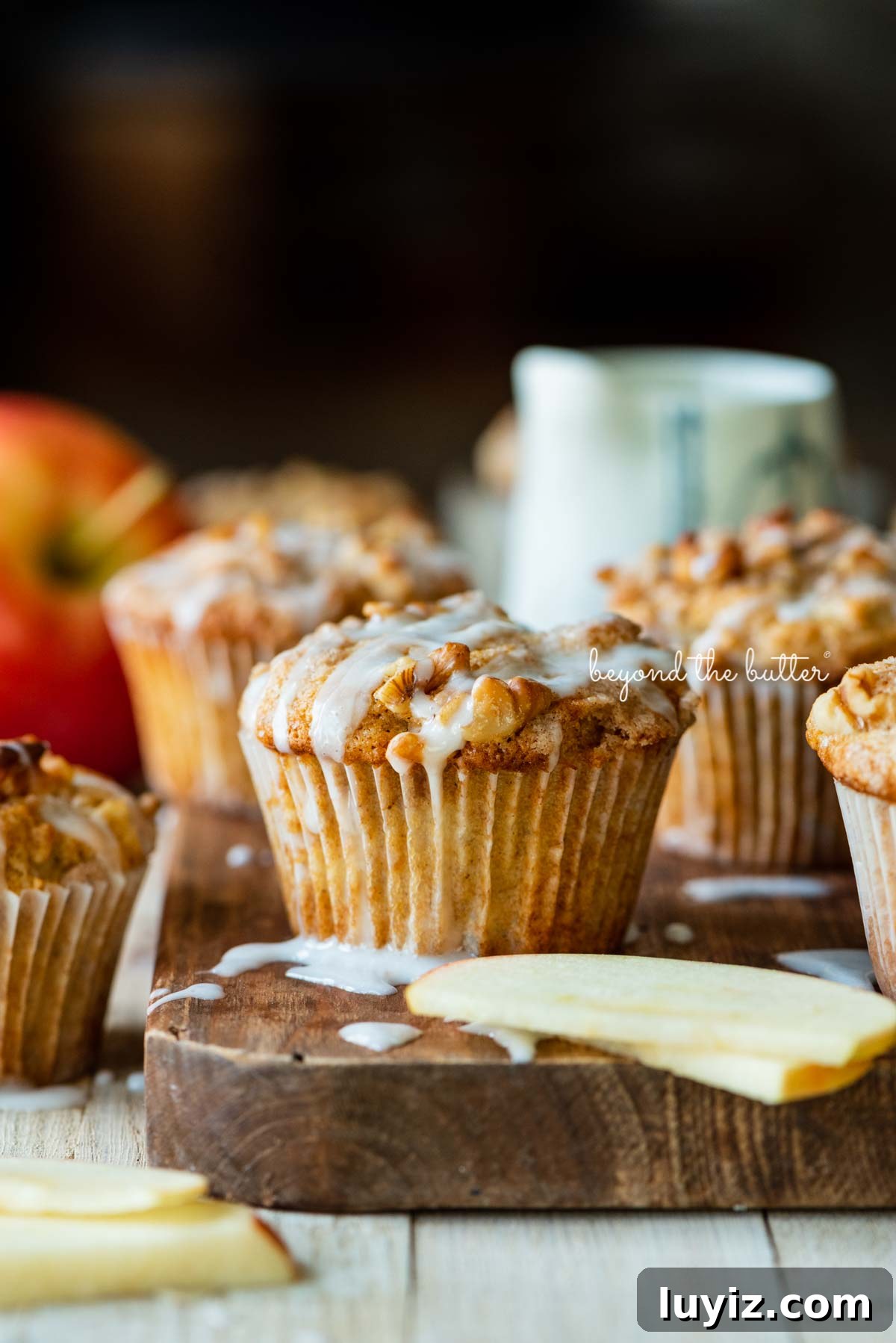 Apple Cinnamon Streusel Muffins Recipe with Crunchy Topping 5 Warm apple cinnamon streusel muffins on a wood cutting board with slices of apples and vanilla glaze