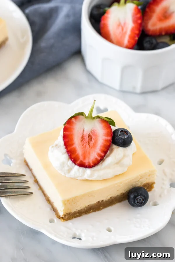 Creamy Cheesecake Bars Recipe for Crowd-Pleasing Desserts 4 Cheesecake square on a plate, topped with cream and berries.