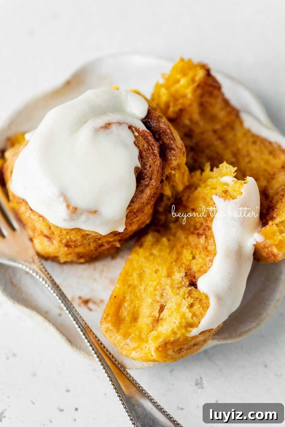 Pumpkin Cinnamon Rolls with Cream Cheese Frosting Recipe 4 Unraveled, half eaten pumpkin cinnamon roll on a dessert plate with small fork on a white marbled background.