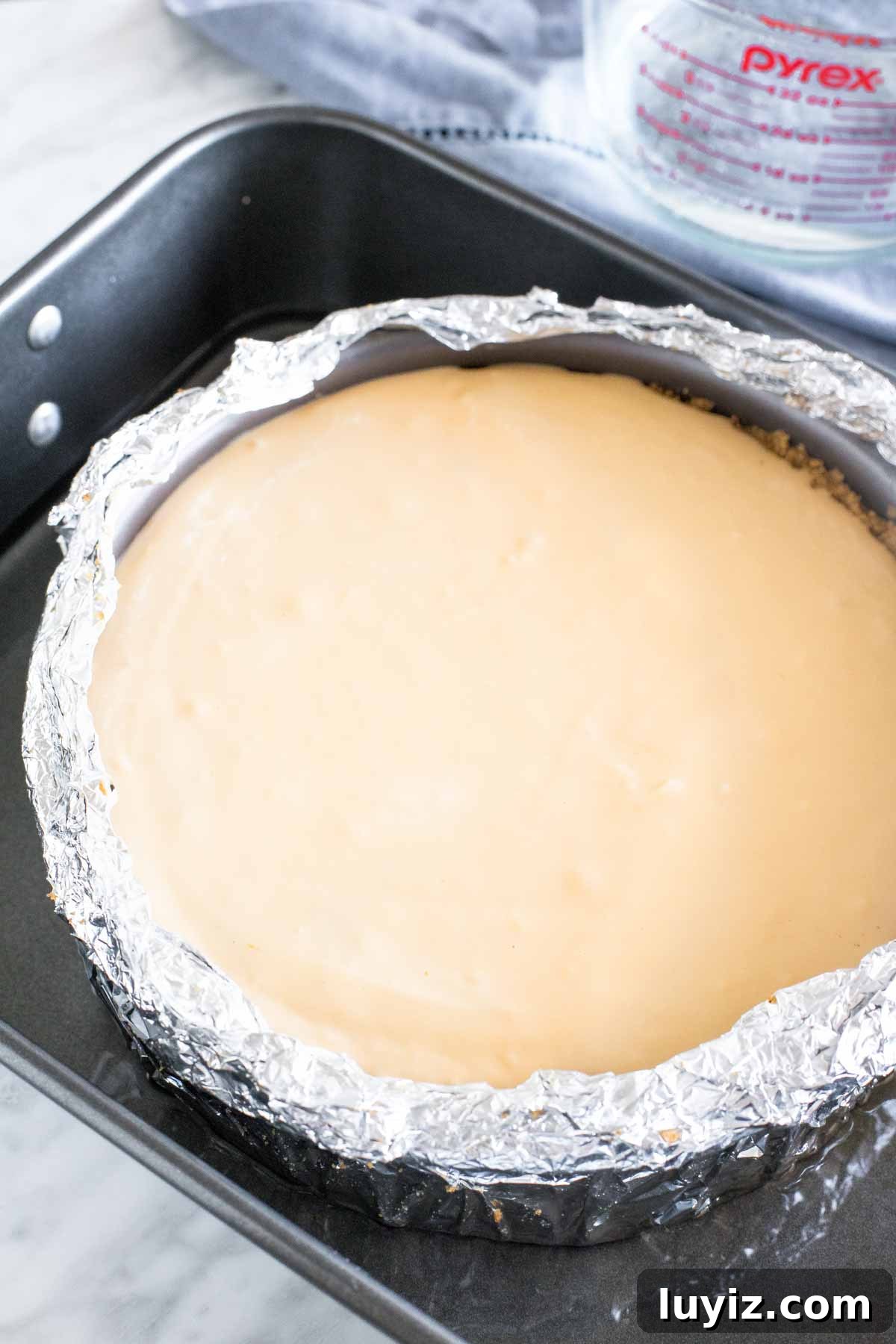 Salted Caramel Apple Cheesecake Recipe with Crunchy Streusel 4 Unbaked cheesecake in a springform pan wrapped in tinfoil in a large roasting pan.