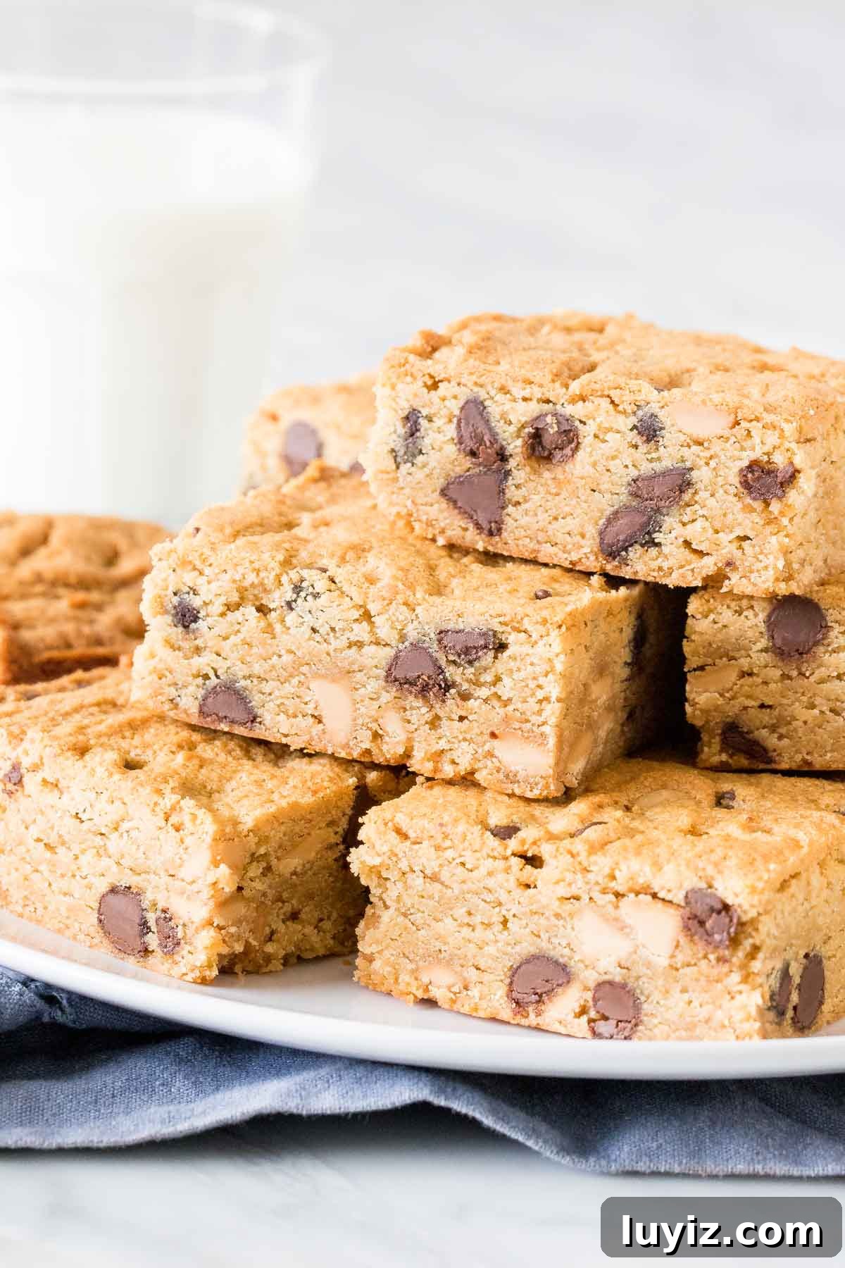 Chewy Peanut Butter Cookie Bars Recipe — Simple Crowd-Pleaser 2 Plate of peanut butter cookie bars stacked one top of each other with glass of milk.