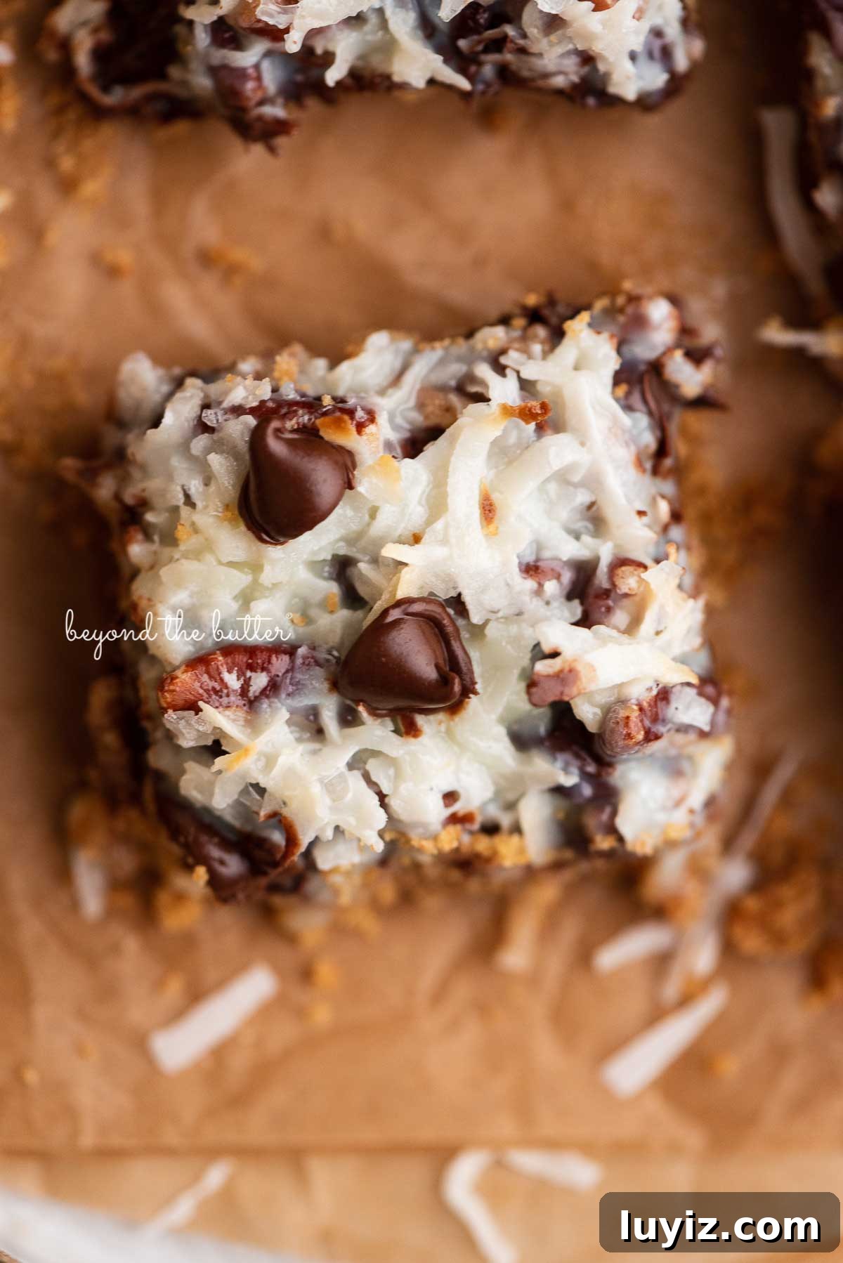 7-Layer Magic Cookie Bars Recipe (Classic Dessert Bars) 6 Magic cookie bars on brown parchment paper | © Beyond the Butter®