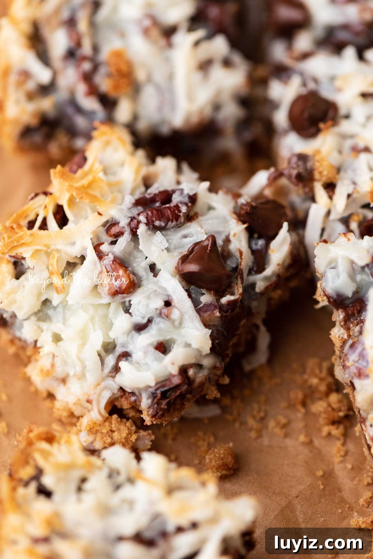 7-Layer Magic Cookie Bars Recipe (Classic Dessert Bars) 7 7 layer magic cookie bars on brown parchment paper | © Beyond the Butter®