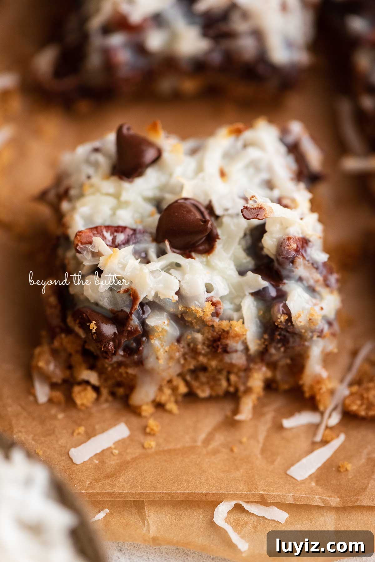 7-Layer Magic Cookie Bars Recipe (Classic Dessert Bars) 9 Sliced magic cookie bars on brown parchment paper | © Beyond the Butter®