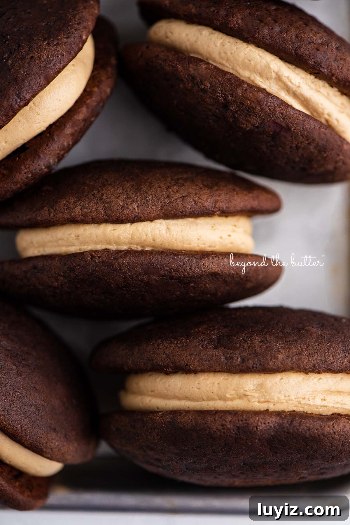 Chocolate Peanut Butter Whoopie Pies Recipe — Soft, Gooey Sandwich Cookies 4 Chocolate peanut butter whoopie pies on a parchment lined baking pan | © Beyond the Butter®