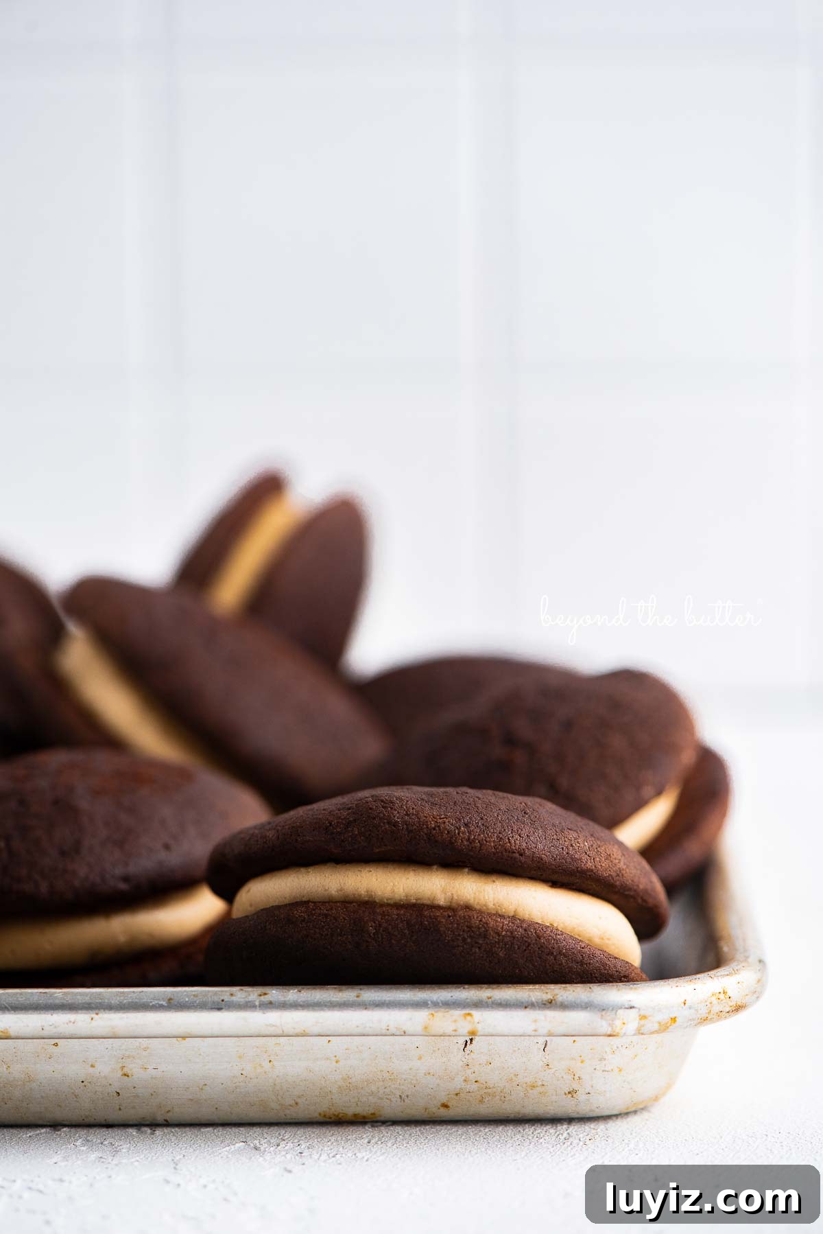 Chocolate Peanut Butter Whoopie Pies Recipe — Soft, Gooey Sandwich Cookies 5 Chocolate peanut butter whoopie pies on a parchment lined baking pan | © Beyond the Butter®