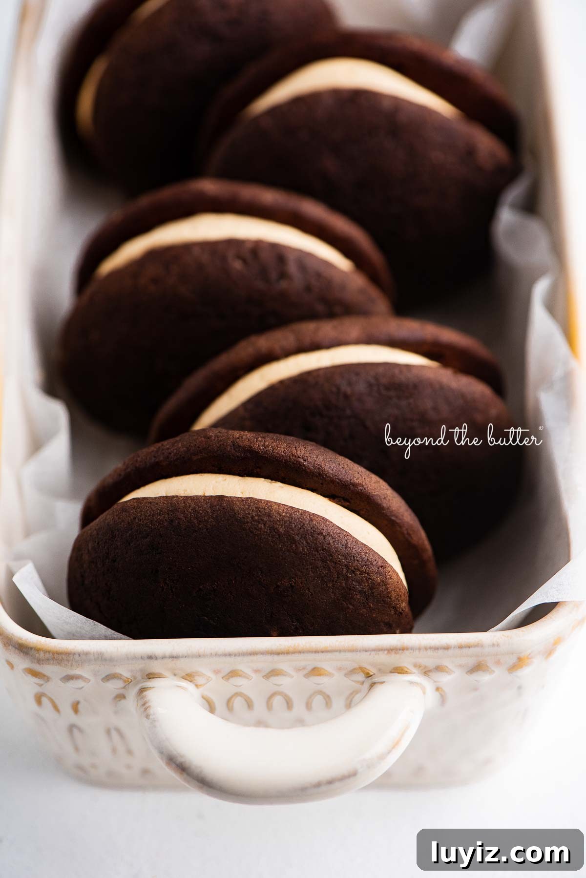 Chocolate Peanut Butter Whoopie Pies Recipe — Soft, Gooey Sandwich Cookies 6 Ceramic loaf dish lined with parchment paper and chocolate peanut butter whoopie pies | © Beyond the Butter®