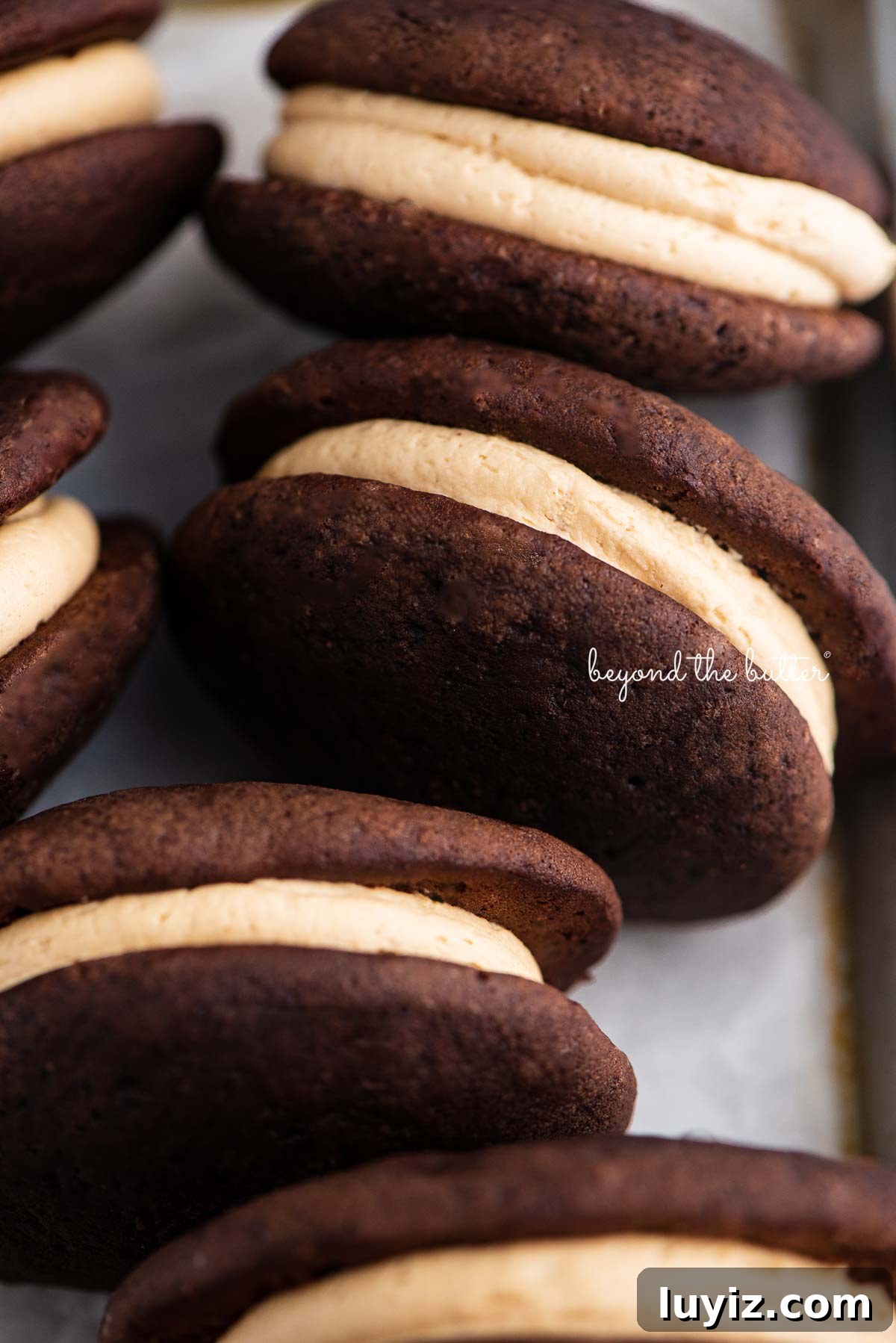 Chocolate Peanut Butter Whoopie Pies Recipe — Soft, Gooey Sandwich Cookies 7 Chocolate peanut butter whoopie pies on a parchment lined baking pan | © Beyond the Butter®